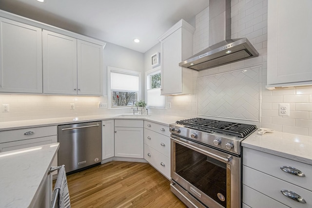 kitchen featuring appliances with stainless steel finishes, light wood-type flooring, white cabinetry, and wall chimney exhaust hood