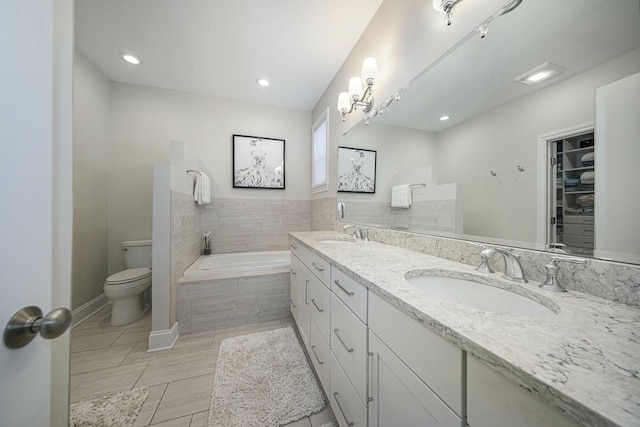 bathroom with a relaxing tiled tub, toilet, and vanity