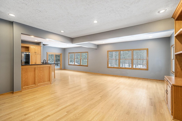 unfurnished living room with a textured ceiling, light hardwood / wood-style floors, and sink