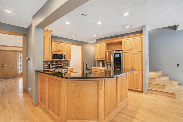 kitchen featuring stainless steel appliances, light hardwood / wood-style floors, light brown cabinetry, backsplash, and a center island with sink