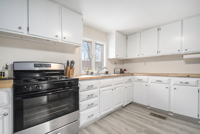 kitchen featuring gas stove, white cabinetry, sink, and light hardwood / wood-style flooring