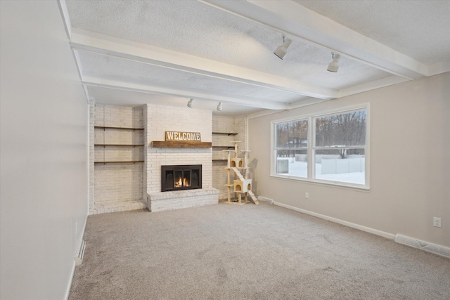 unfurnished living room with a textured ceiling, carpet flooring, rail lighting, and beam ceiling