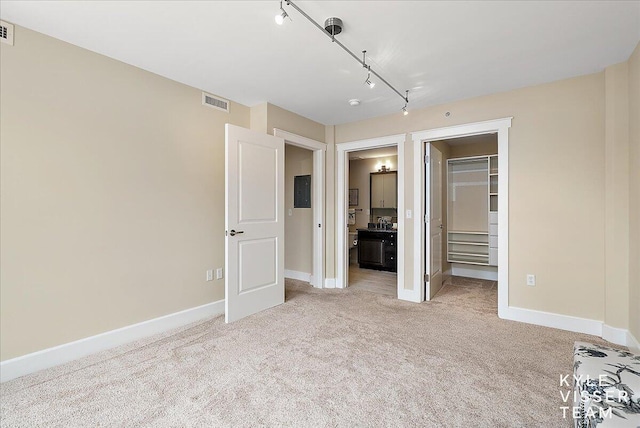 unfurnished bedroom with a closet, rail lighting, light colored carpet, electric panel, and a walk in closet