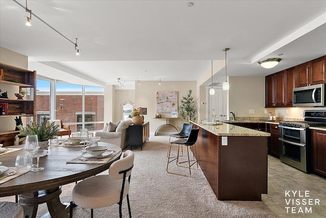 kitchen featuring decorative light fixtures, light stone counters, a kitchen breakfast bar, light carpet, and appliances with stainless steel finishes