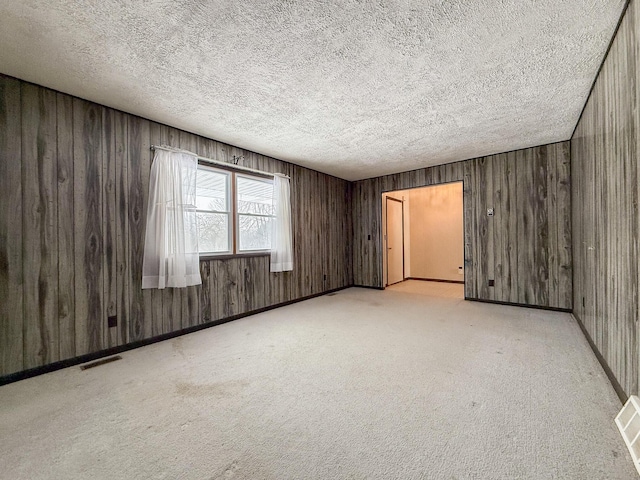 spare room featuring a textured ceiling, light colored carpet, and wooden walls