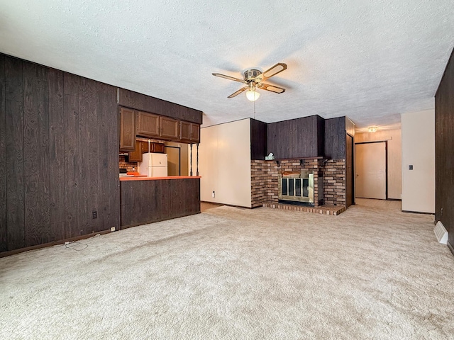 unfurnished living room featuring ceiling fan, a brick fireplace, light colored carpet, a textured ceiling, and wooden walls