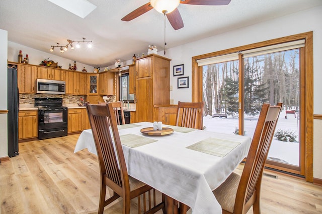 dining space with light hardwood / wood-style floors, ceiling fan, and vaulted ceiling with skylight