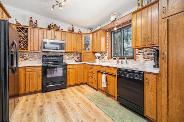 kitchen with backsplash, light hardwood / wood-style floors, black appliances, and sink