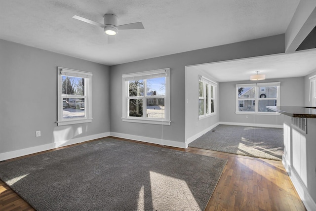 unfurnished living room featuring ceiling fan, dark wood-type flooring, and a textured ceiling