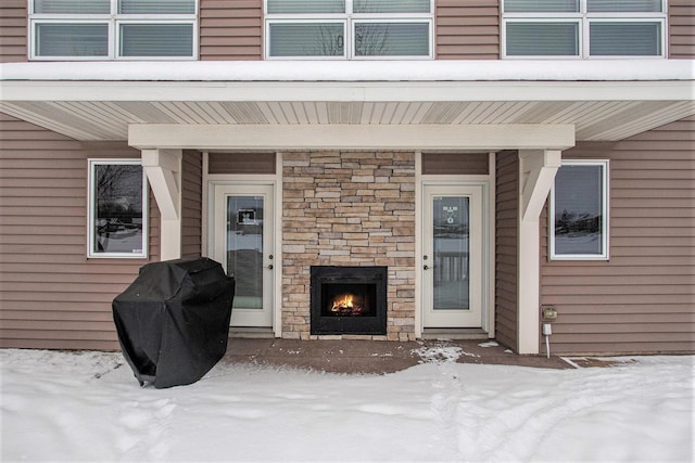 snow covered property entrance featuring an outdoor stone fireplace