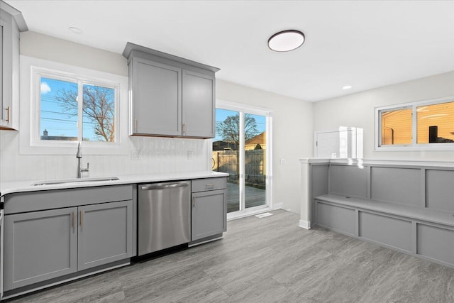 kitchen featuring tasteful backsplash, gray cabinets, dishwasher, and sink