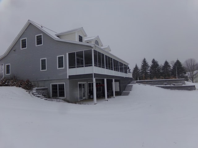 snow covered rear of property with a sunroom