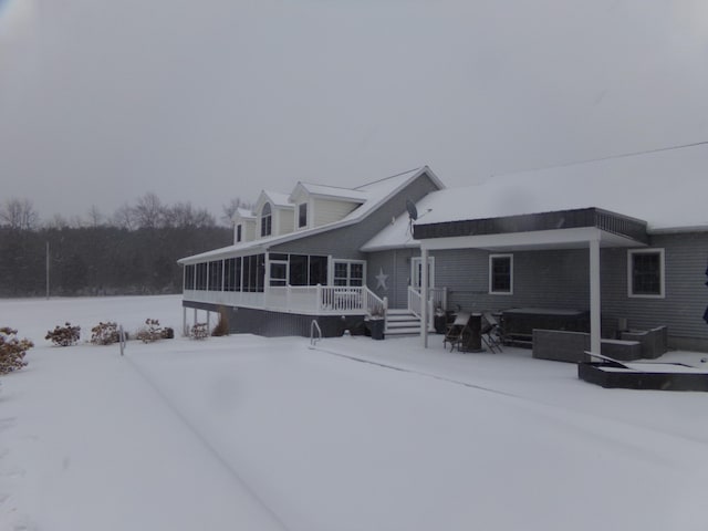 snow covered rear of property featuring a hot tub and a sunroom