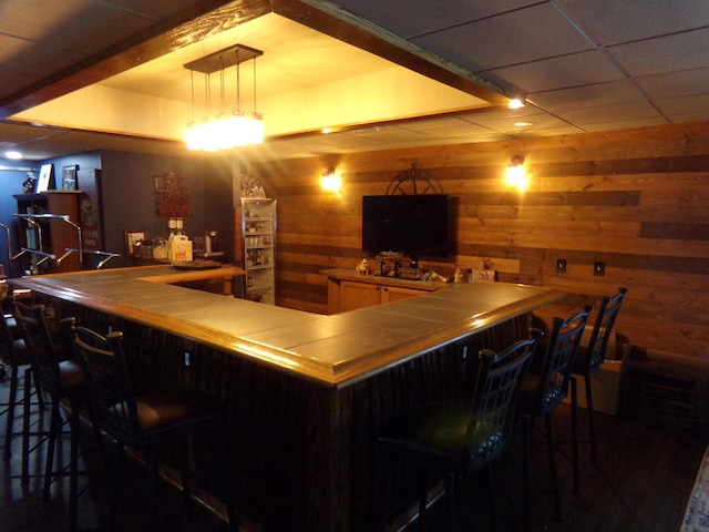 bar featuring decorative light fixtures, wood walls, and a drop ceiling