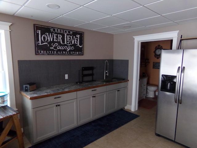 kitchen with sink, white cabinetry, a drop ceiling, decorative backsplash, and stainless steel fridge