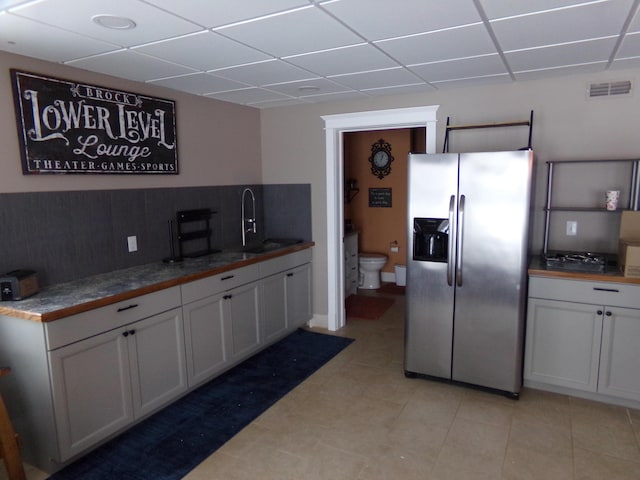 kitchen with sink, white cabinets, a drop ceiling, and stainless steel fridge