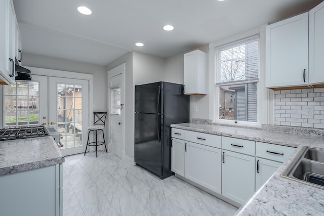 kitchen featuring french doors, sink, decorative backsplash, black refrigerator, and white cabinets