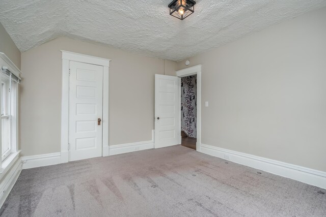 unfurnished bedroom with carpet, a textured ceiling, and vaulted ceiling