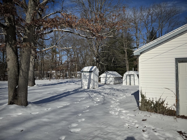 yard layered in snow featuring a garage and an outbuilding