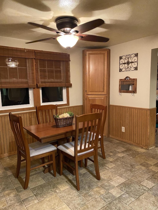 dining space featuring wooden walls, a textured ceiling, and ceiling fan