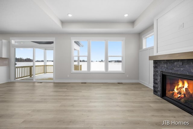 unfurnished living room featuring a tray ceiling, a fireplace, light hardwood / wood-style floors, and a wealth of natural light