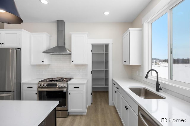 kitchen with sink, white cabinetry, light hardwood / wood-style flooring, stainless steel appliances, and wall chimney range hood