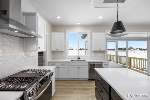 kitchen with sink, wall chimney range hood, pendant lighting, stainless steel appliances, and white cabinets