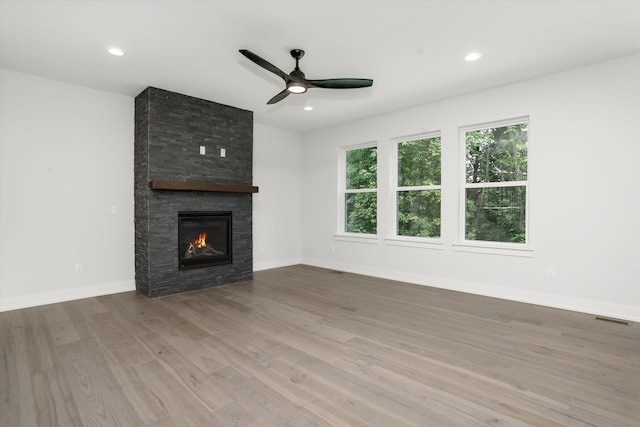 unfurnished living room featuring hardwood / wood-style flooring, ceiling fan, and a large fireplace