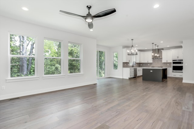 unfurnished living room with wood-type flooring, ceiling fan with notable chandelier, and sink