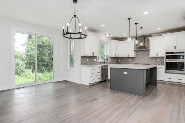 kitchen with white cabinetry, wall chimney exhaust hood, decorative light fixtures, a kitchen island, and appliances with stainless steel finishes