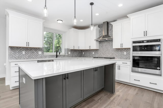 kitchen featuring wall chimney exhaust hood, a kitchen island, decorative light fixtures, gray cabinets, and white cabinets