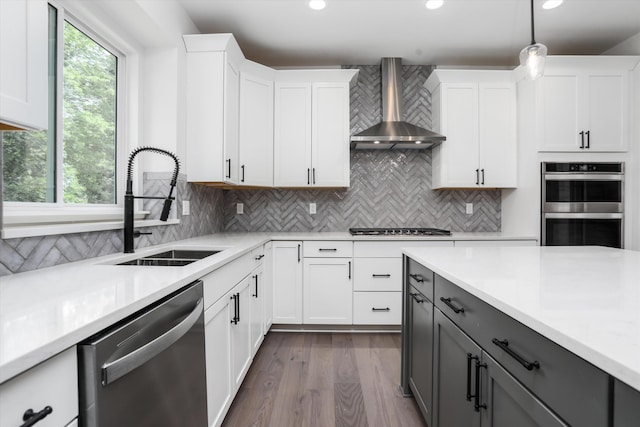 kitchen featuring gray cabinetry, pendant lighting, wall chimney range hood, appliances with stainless steel finishes, and white cabinetry