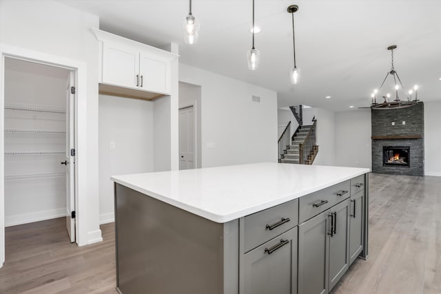 kitchen featuring pendant lighting, white cabinets, light wood-type flooring, and a fireplace