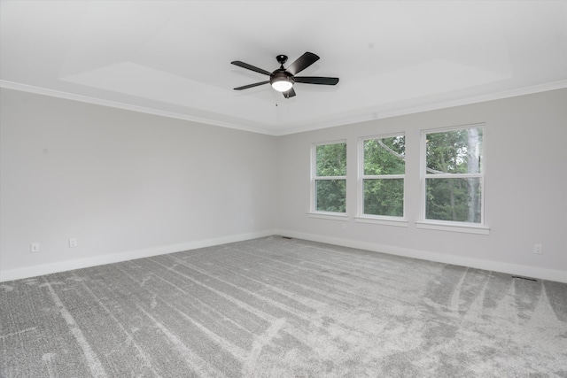 empty room with ceiling fan, a raised ceiling, light carpet, and crown molding