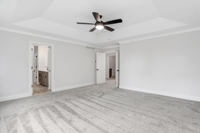 unfurnished bedroom featuring light carpet, ensuite bathroom, crown molding, ceiling fan, and a tray ceiling