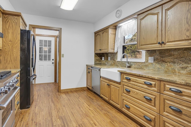 kitchen featuring light stone countertops, appliances with stainless steel finishes, sink, backsplash, and light wood-type flooring