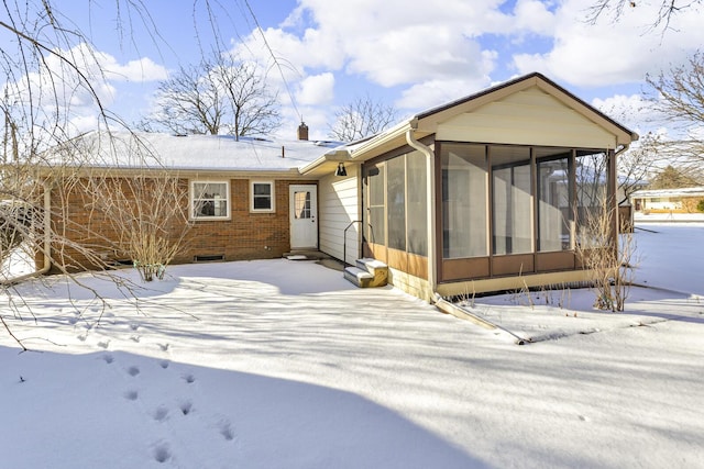 snow covered house featuring a sunroom