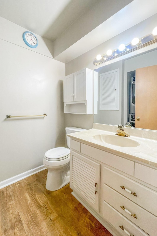 bathroom featuring vanity, toilet, stacked washing maching and dryer, and wood-type flooring