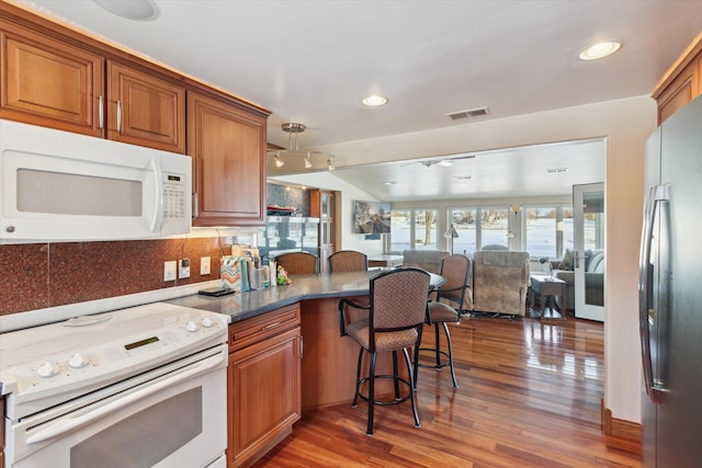 kitchen featuring white appliances, a kitchen breakfast bar, hardwood / wood-style floors, and backsplash