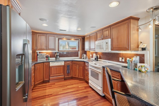 kitchen featuring sink, white appliances, light wood-type flooring, tasteful backsplash, and dark stone counters