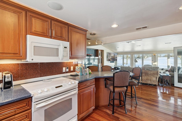 kitchen with white appliances, dark stone countertops, backsplash, dark hardwood / wood-style flooring, and a breakfast bar