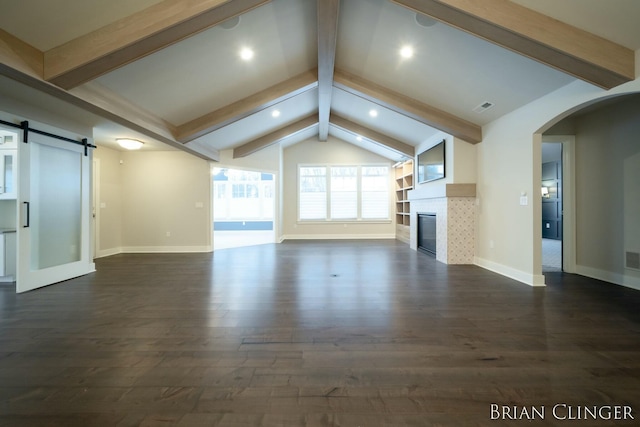 unfurnished living room with a barn door, dark hardwood / wood-style floors, vaulted ceiling with beams, and a fireplace