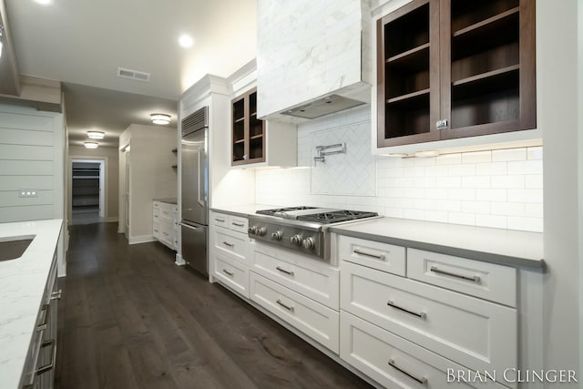 kitchen featuring appliances with stainless steel finishes, tasteful backsplash, light stone counters, white cabinets, and custom exhaust hood