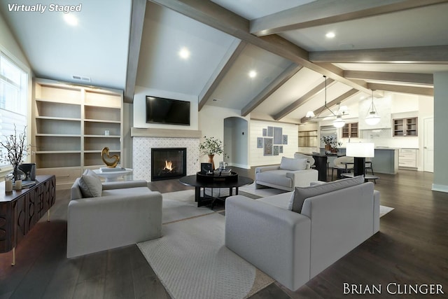 living room featuring dark hardwood / wood-style floors, a tiled fireplace, and vaulted ceiling with beams