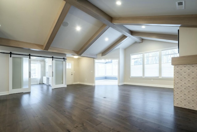 unfurnished living room featuring a healthy amount of sunlight, a barn door, dark hardwood / wood-style flooring, and vaulted ceiling with beams