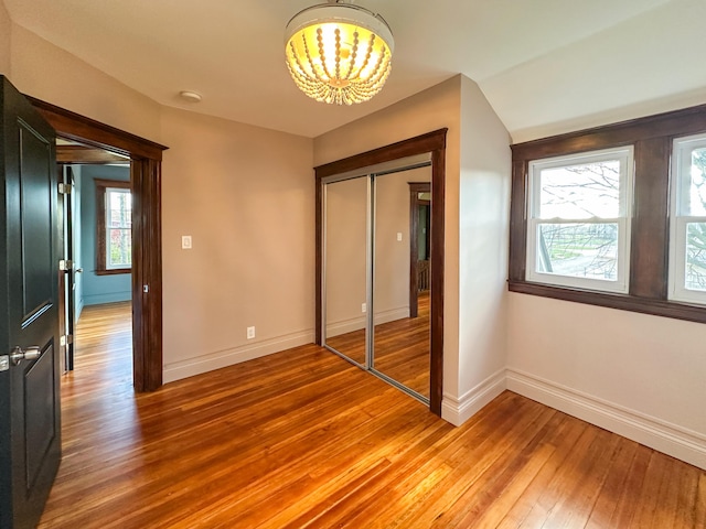 unfurnished bedroom featuring an inviting chandelier, a closet, and wood-type flooring