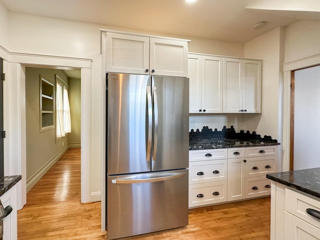 kitchen with dark stone counters, stainless steel fridge, white cabinetry, and light wood-type flooring