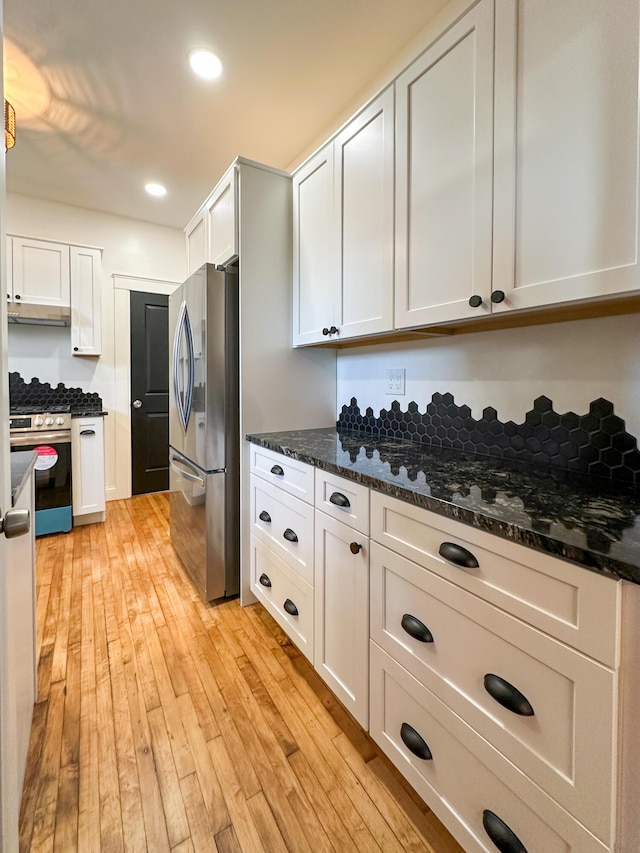 kitchen with dark stone counters, light wood-type flooring, appliances with stainless steel finishes, and white cabinetry