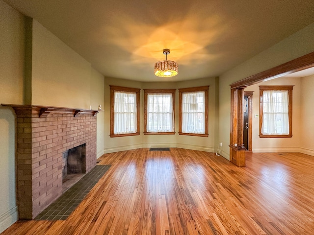 unfurnished living room with a brick fireplace, a wealth of natural light, and hardwood / wood-style flooring