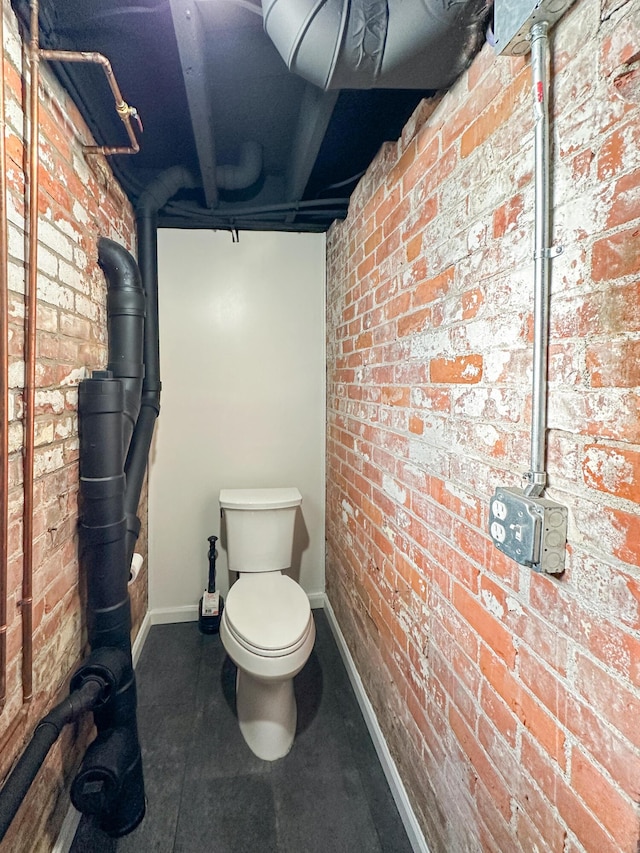 bathroom featuring brick wall and toilet